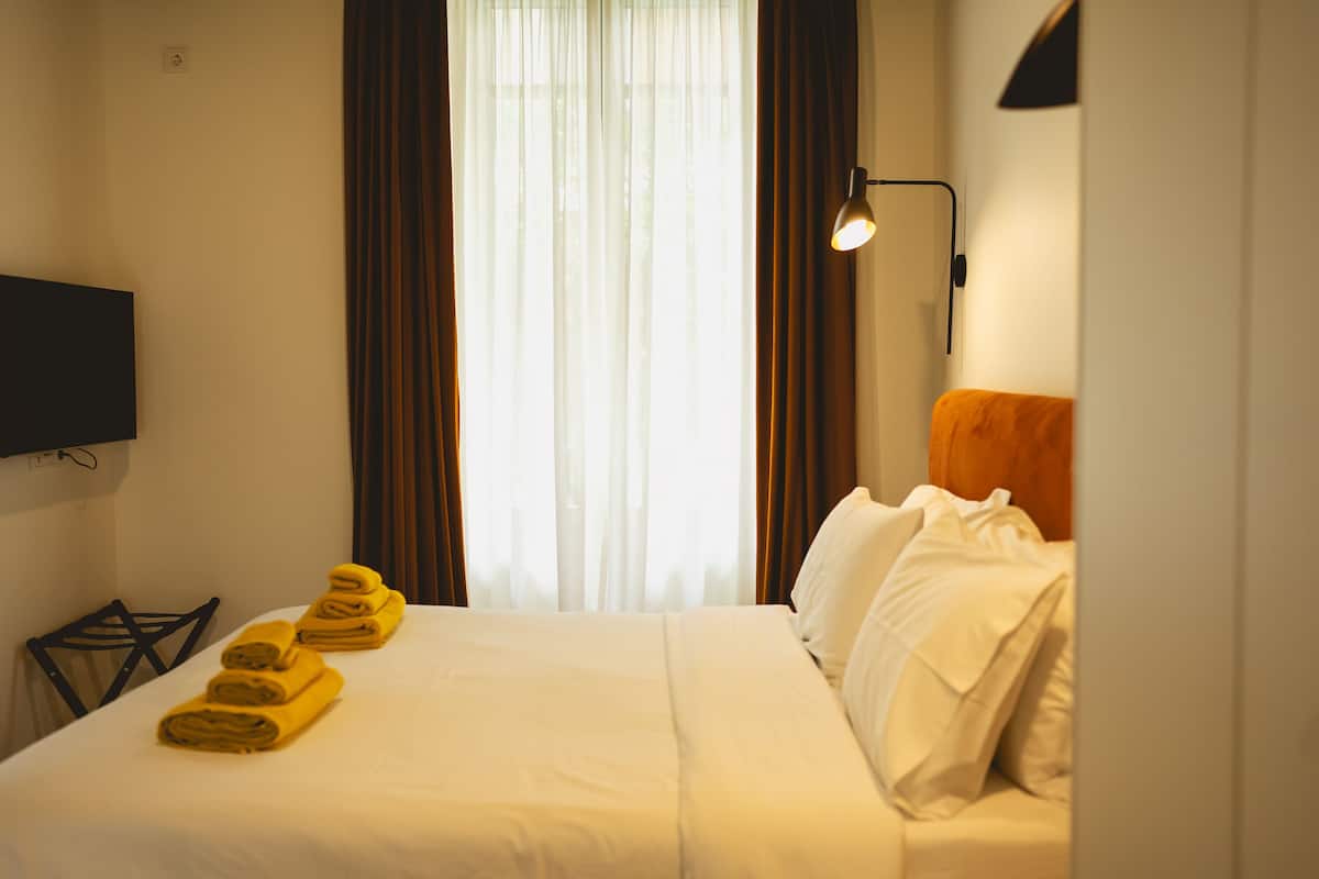 Habitació d'hotel amb un llit, una televisió, una làmpada i una finestra amb cortines.