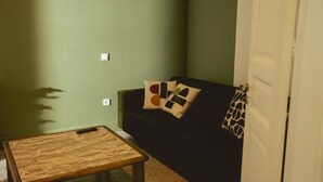 Una sala de estar con una mesa de centro de madera, un sofá de color oscuro con cojines estampados y una puerta cerrada.