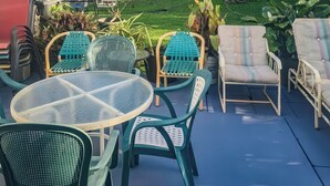 An outdoor patio with round tables and chairs, surrounded by lush greenery and tall trees. - Studio Efficiency Apartment (Port Saint Lucie)