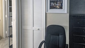 Ein Zimmer mit geschlossenem weißen Kleiderschrank, einem gerahmten Bild an der Wand und einem schwarzen Bürostuhl.