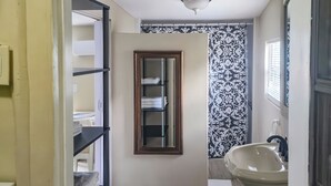 A bathroom with a sink, mirror, patterned wallpaper, and a tiled floor. - Studio Efficiency Apartment (Port Saint Lucie)