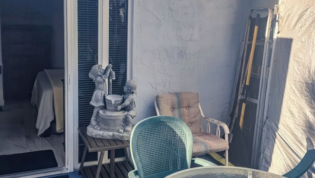 A patio area with a glass table surrounded by chairs, a statue, and a cushioned chair. - Studio Efficiency Apartment (Port Saint Lucie)