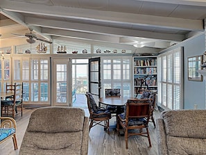 A spacious dining area with a round table and chairs, a bookshelf, and a view through large windows. - Dog Friendly- Oceanfront Litchfield Beach! The Flag House - Traumerei (Pawleys Island)