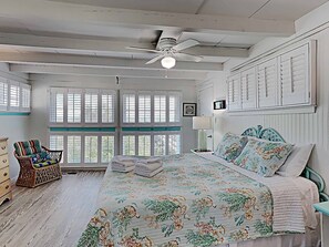 A bedroom with a bed, a chair, a dresser, a ceiling fan, and a window with shutters. - Dog Friendly- Oceanfront Litchfield Beach! The Flag House - Traumerei (Pawleys Island)