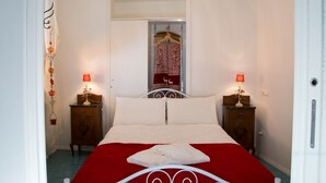 A bed with a red bedspread, two bedside tables with lamps, a wooden wardrobe, and a mirror with a red curtain. - Casa Gargano Ravello Amalfi Coast (Ravello)