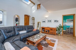 Ein Wohnzimmer mit einer Ledersofa, einem Holztisch, einem Schrank und einer durch einen offenen Durchgang sichtbaren Küche.