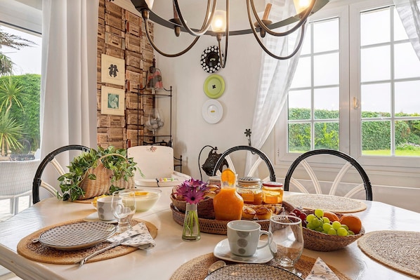 Une table de petit-déjeuner dressée avec des assiettes, des verres et un panier de fruits, donnant sur un paysage verdoyant.