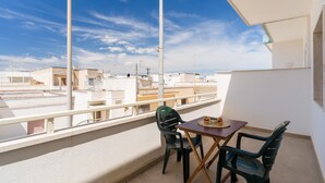 Varanda com mesa e cadeiras, vista para um horizonte urbano com edifícios e céu claro.