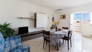 Uma sala de jantar com uma mesa posta para quatro pessoas, um sofá, uma TV e um armário.