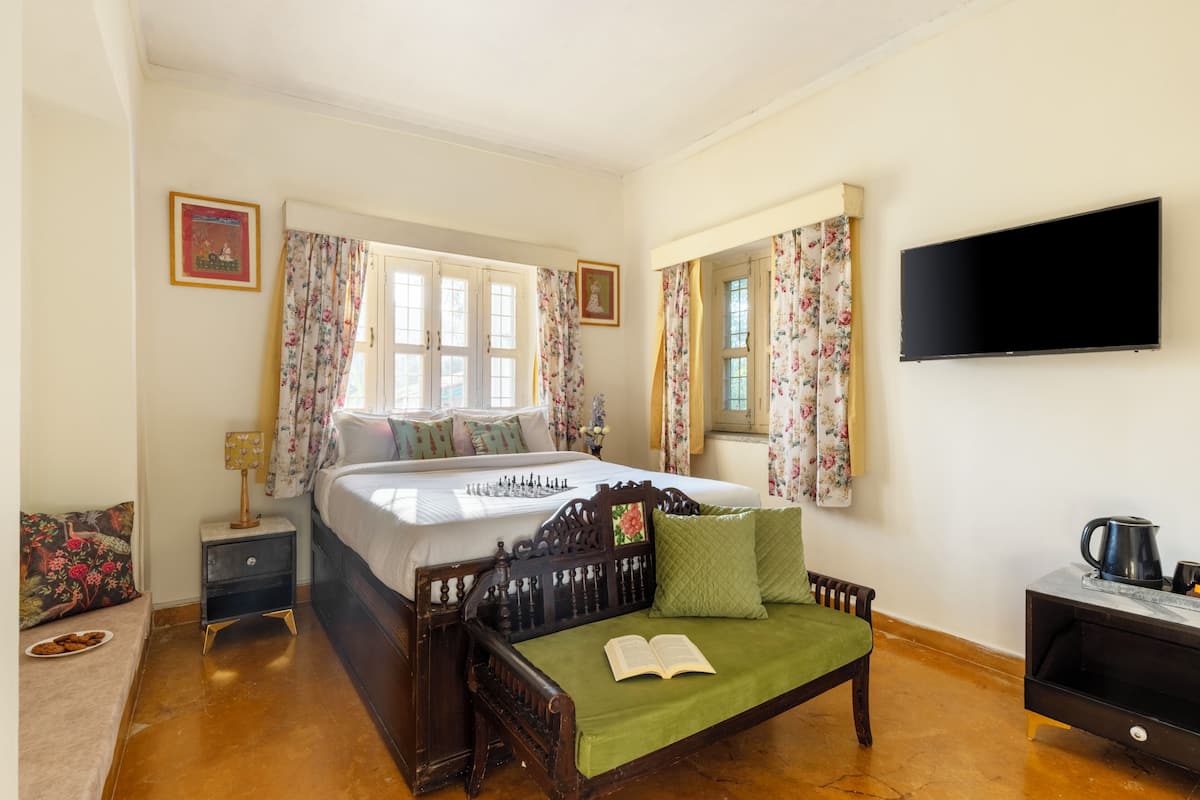 A bedroom with a bed, a green sofa, a nightstand, a TV, and a window with curtains.