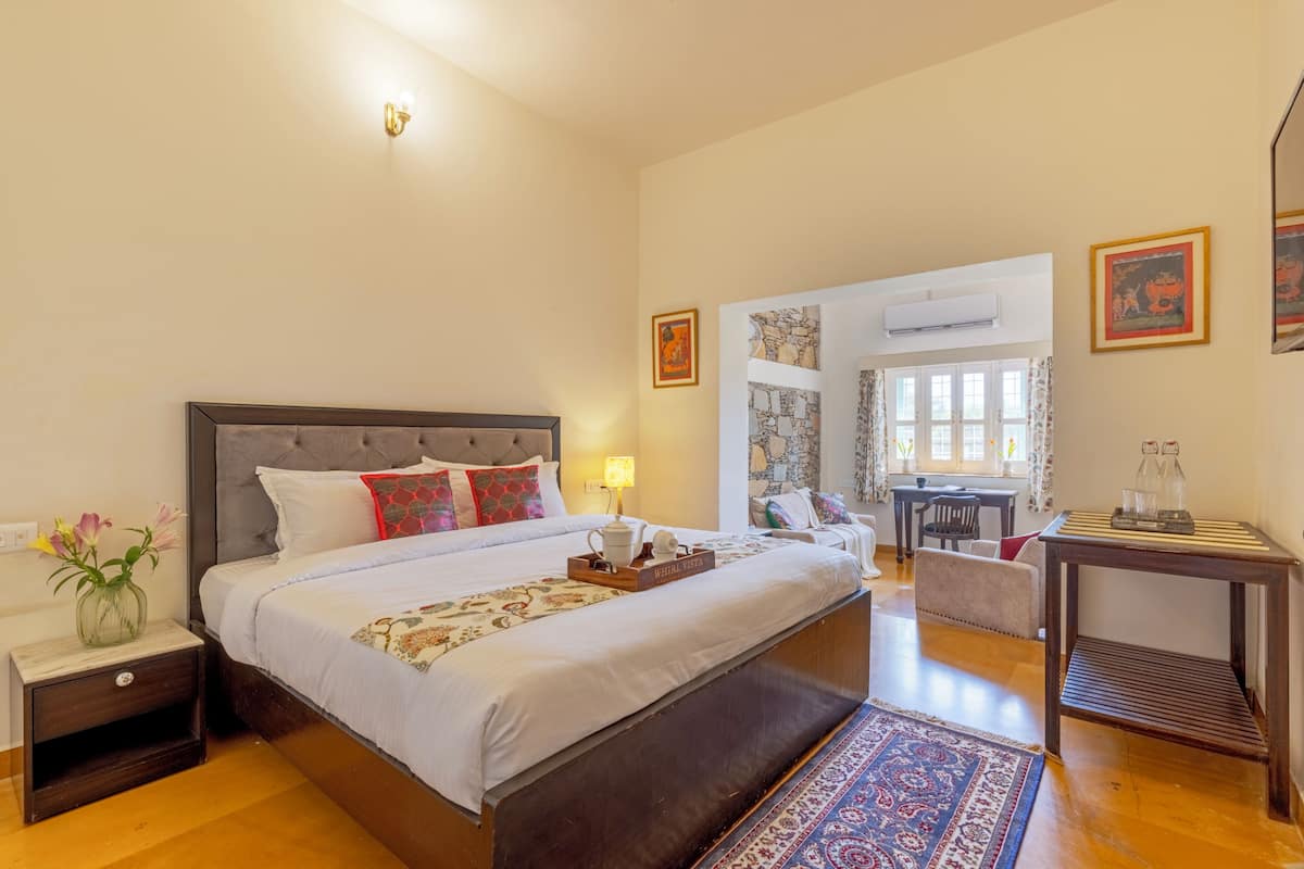 A hotel room with a bed, bedside table, lamp, and a small table with decorative items.