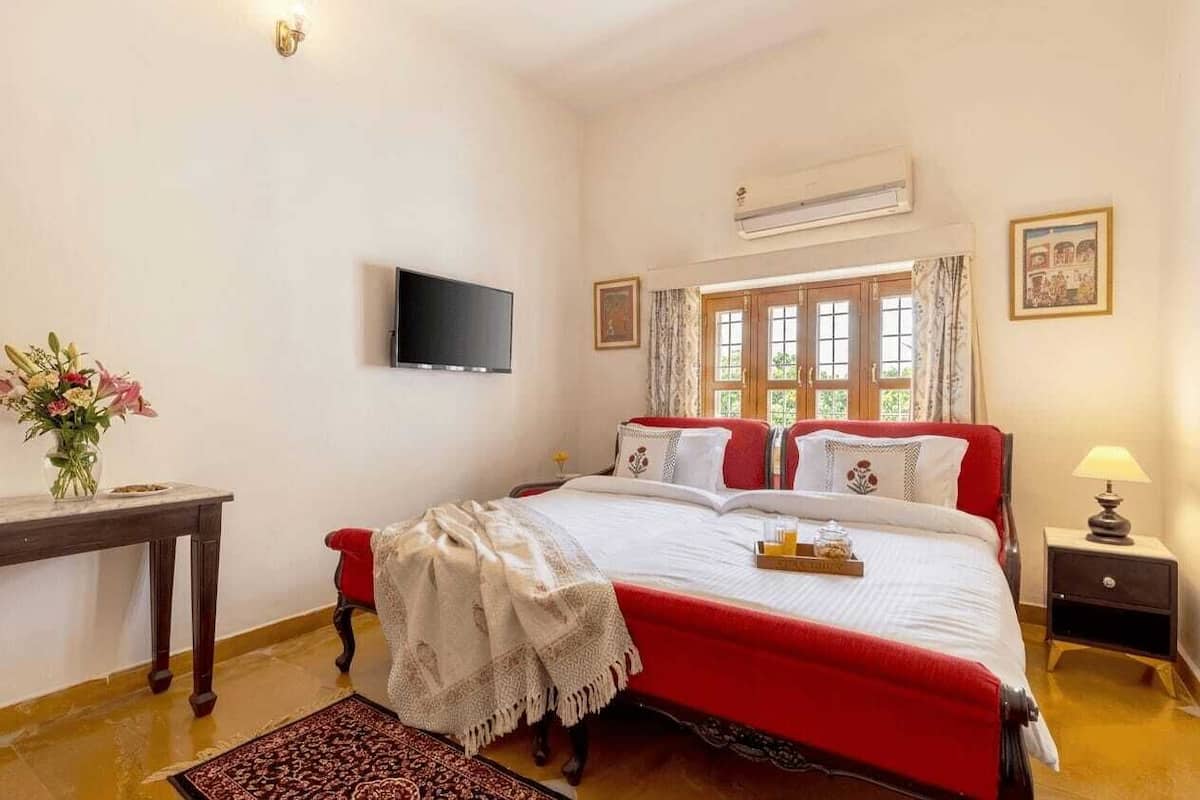 A bedroom with a bed, a TV, a window, a bedside table, and a lamp.