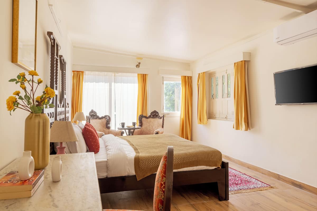 A hotel room with a bed, a desk with a lamp, a chair, a TV, and a window with curtains.