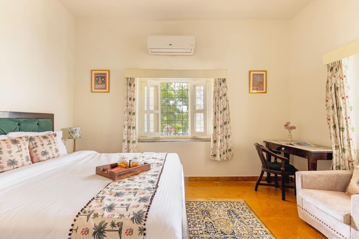 Un dormitorio con una cama, un escritorio, una silla, un ventanal con cortinas y aire acondicionado.