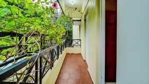 A narrow corridor with a metal railing on one side, a wooden door on the other, and a view of greenery outside. - Alaya Stays Saffron Breeze 4 BHK Apt (Bengaluru)