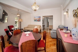 Un coin repas avec une table ronde, des chaises, un lustre et un canapé en arrière-plan.