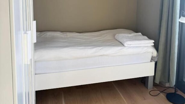 A small, single-bed room with a wooden floor, a white bed, and a curtain on the window. - Room-serene Guest Room Escape in Asker, (Asker)