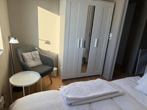 Quarto de hotel com cama, uma cadeira, uma mesinha e um guarda-roupa.