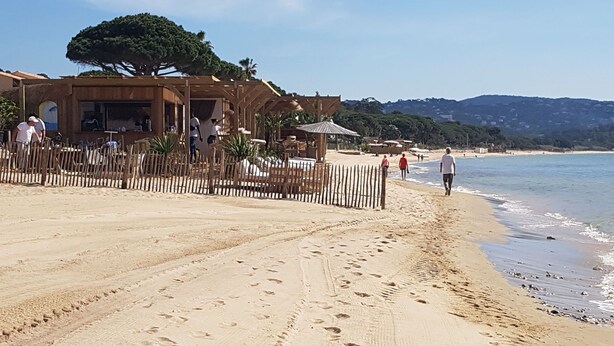 Een strand met een houten constructie, een omheind gebied en voetafdrukken in het zand.