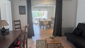 Een woonkamer met een eethoek, een zwarte bank, een houten eettafel en een potplant.