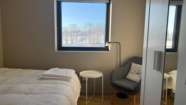 Un dormitorio con cama, una silla, una mesita, una ventana y una puerta.