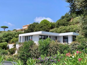 Ein modernes, zweistöckiges Haus mit weißer Fassade, umgeben von üppiger Vegetation und blühenden Pflanzen.