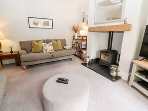Una sala de estar con sofá, reposapiés, chimenea, estantería y televisor.