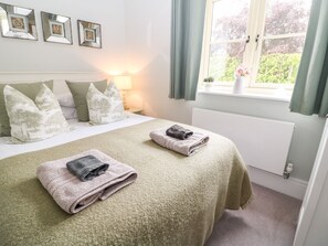 A neatly made bed with pillows, a lamp, and a window with curtains. - East View (Cheltenham)