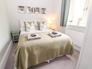A neatly made bed with a green blanket, a bedside lamp, and a window with curtains. - East View (Cheltenham)
