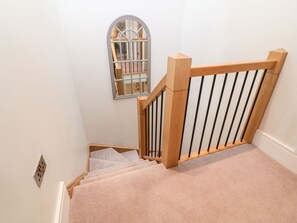A staircase with a wooden handrail and black balusters, carpeted steps, and a wall-mounted light switch. - East View (Cheltenham)