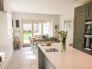 Una cocina moderna con una isla central, un área de comedor con sillas y una mesa, y vistas al jardín trasero.