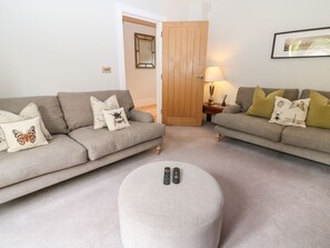 A living room with two sofas, a round ottoman, a wooden door, a lamp, and a framed picture on the wall. - East View (Cheltenham)