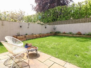 A backyard with a grassy lawn, a wooden deck, a fire pit, and a white chair. - East View (Cheltenham)