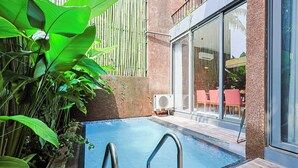 A swimming pool with metal ladders, surrounded by lush green plants and a modern building with large windows and red chairs. - ELIVAAS 3 BHK With Private Pool and Gazebo | Terraces Villa Luxe (Marra)