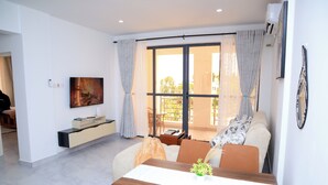 A modern living room with a dining table, sofa, and a TV mounted on the wall.