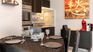 A dining area with a table set for four, a kitchen with modern appliances, and a large abstract painting on the wall. - Gîte Douceur de Vivre - Marais: Lake View, Shared Pool & Wi-Fi (Saint-Avaugourd-des-Landes)