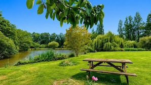 A picnic table in a park with a lake, trees, and grass. - Gîte Douceur de Vivre - Marais: Lake View, Shared Pool & Wi-Fi (Saint-Avaugourd-des-Landes)