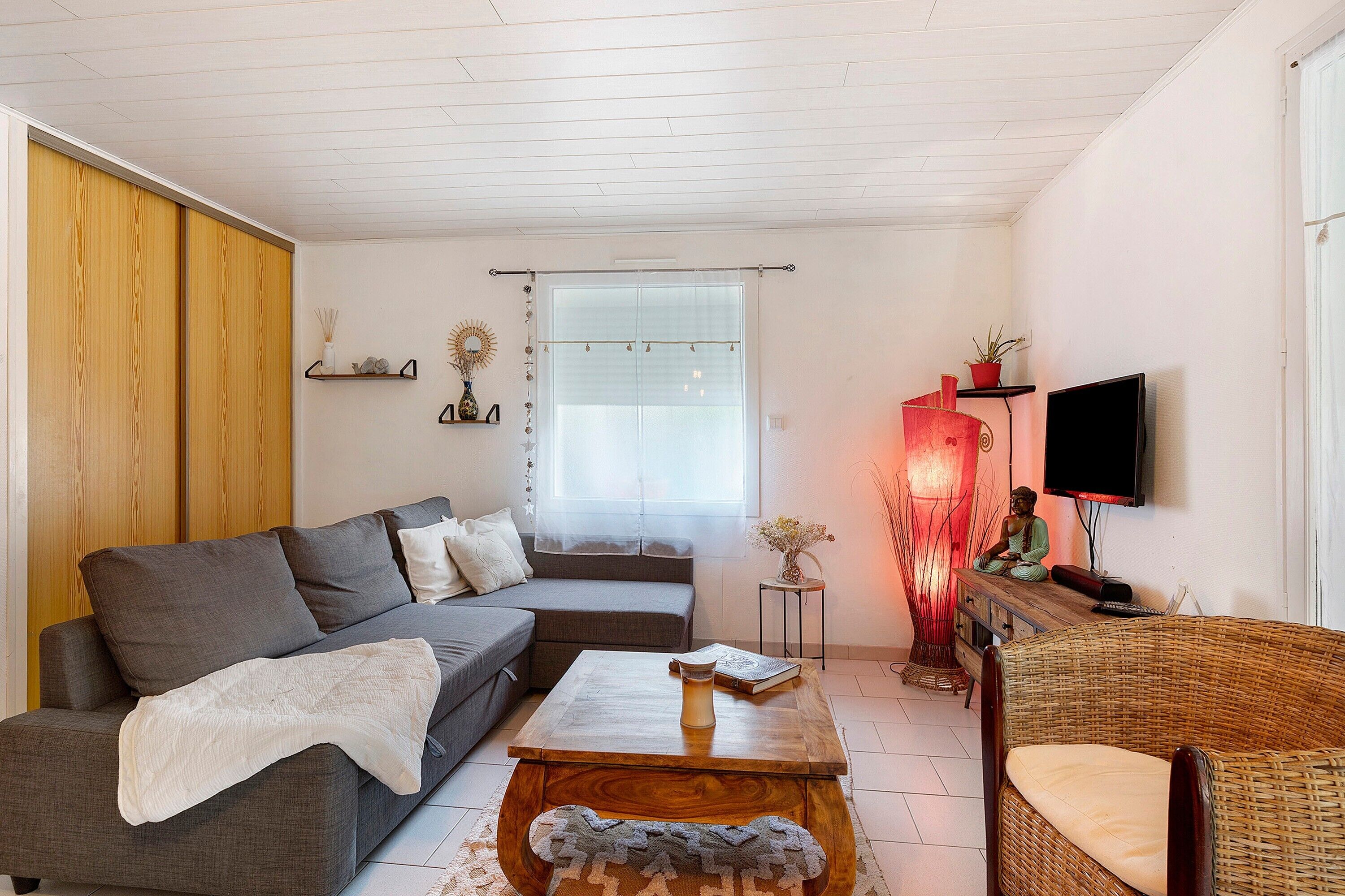Een woonkamer met een bank, een salontafel, een rieten stoel, een televisie en een raam met gordijnen.