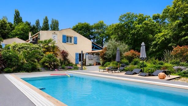 A swimming pool with lounge chairs and umbrellas, surrounded by greenery and a building with blue shutters. - Gîte Douceur de Vivre - Marais: Lake View, Shared Pool & Wi-Fi (Saint-Avaugourd-des-Landes)