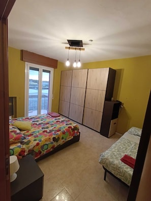 A bedroom with a bed, a wardrobe, a desk, and a window.