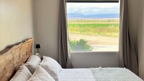 A bedroom with a bed, a headboard, a lamp, and a window with curtains.