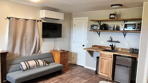 A compact living space with a sofa, kitchenette, TV, and wooden flooring.
