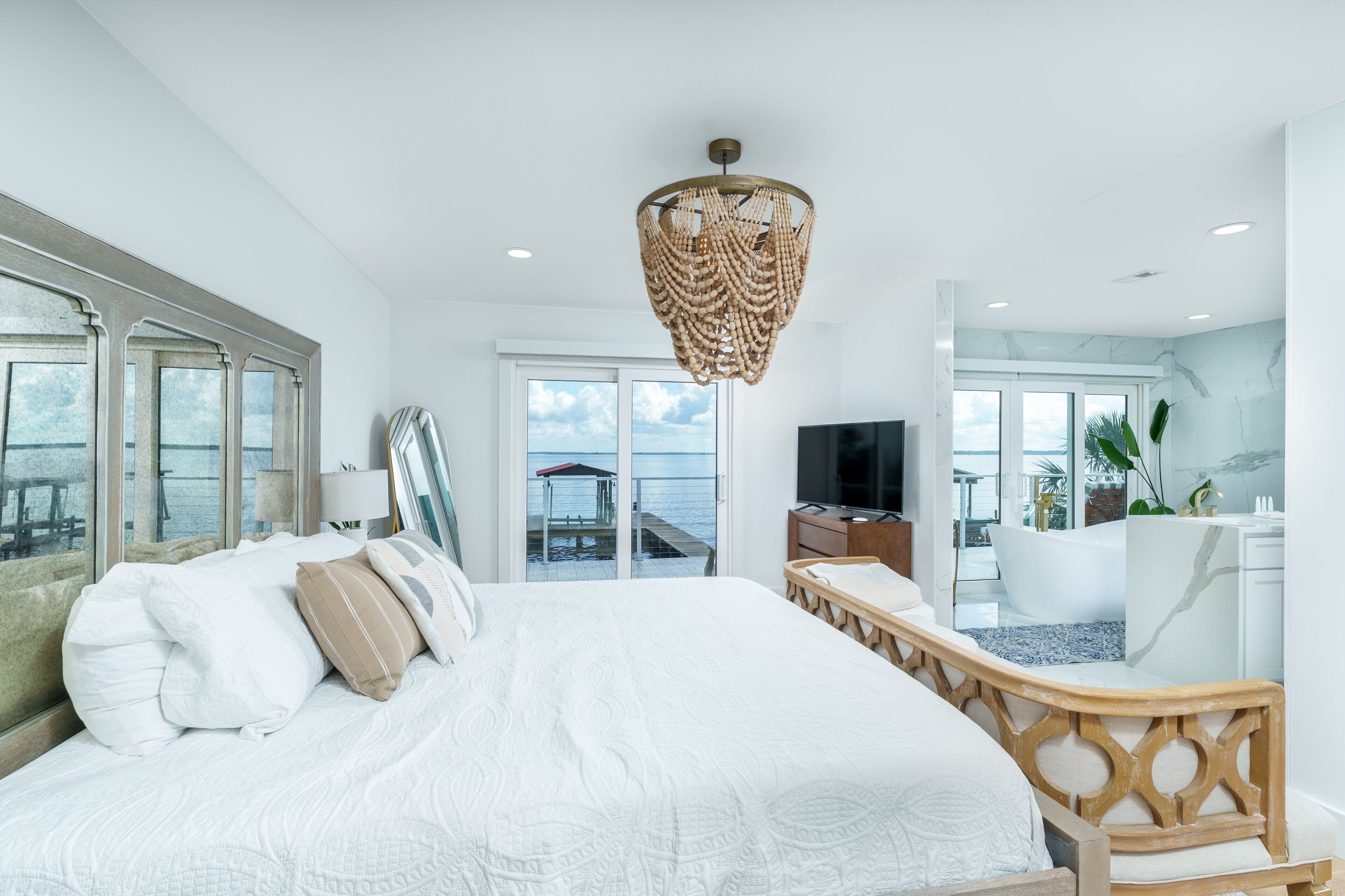 A modern hotel room with a large bed, a television, a balcony with a view of the sea, and a bathroom with a bathtub.