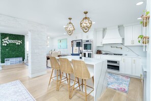 A modern kitchen with white cabinetry, a central island with bar stools, and a green wall with a floral design. - THE BAYFRONT HAVEN Private Dock Sauna Pet-Friendly Luxury Destin 30A Retreat (Santa Rosa Beach)