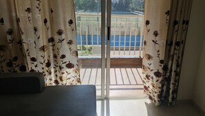 Una habitación con cama, ventana con cortinas florales y vista a una piscina y zona exterior.