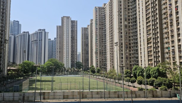 Un barrio residencial con edificios de apartamentos, una cancha deportiva cercada y árboles.