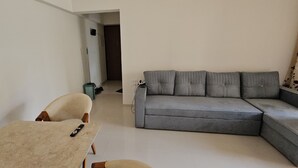 Una sala de estar con un sofá seccional gris, un sillón color beige y una mesita con un control remoto.