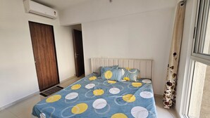 Un dormitorio con cama, ventana con cortinas, puerta y unidad de aire acondicionado.