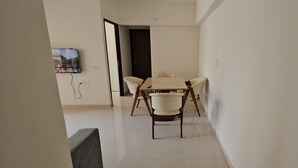Un área de comedor con una mesa y sillas, un televisor montado en la pared y una puerta que da a otra habitación.
