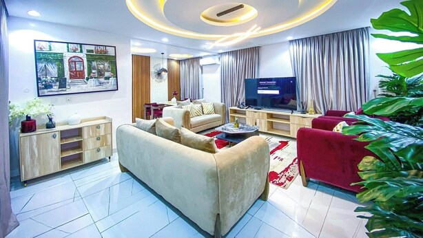 A modern living room with a sofa, TV, and a decorative ceiling light. - THE 81 APARTMENTS (Lagos)